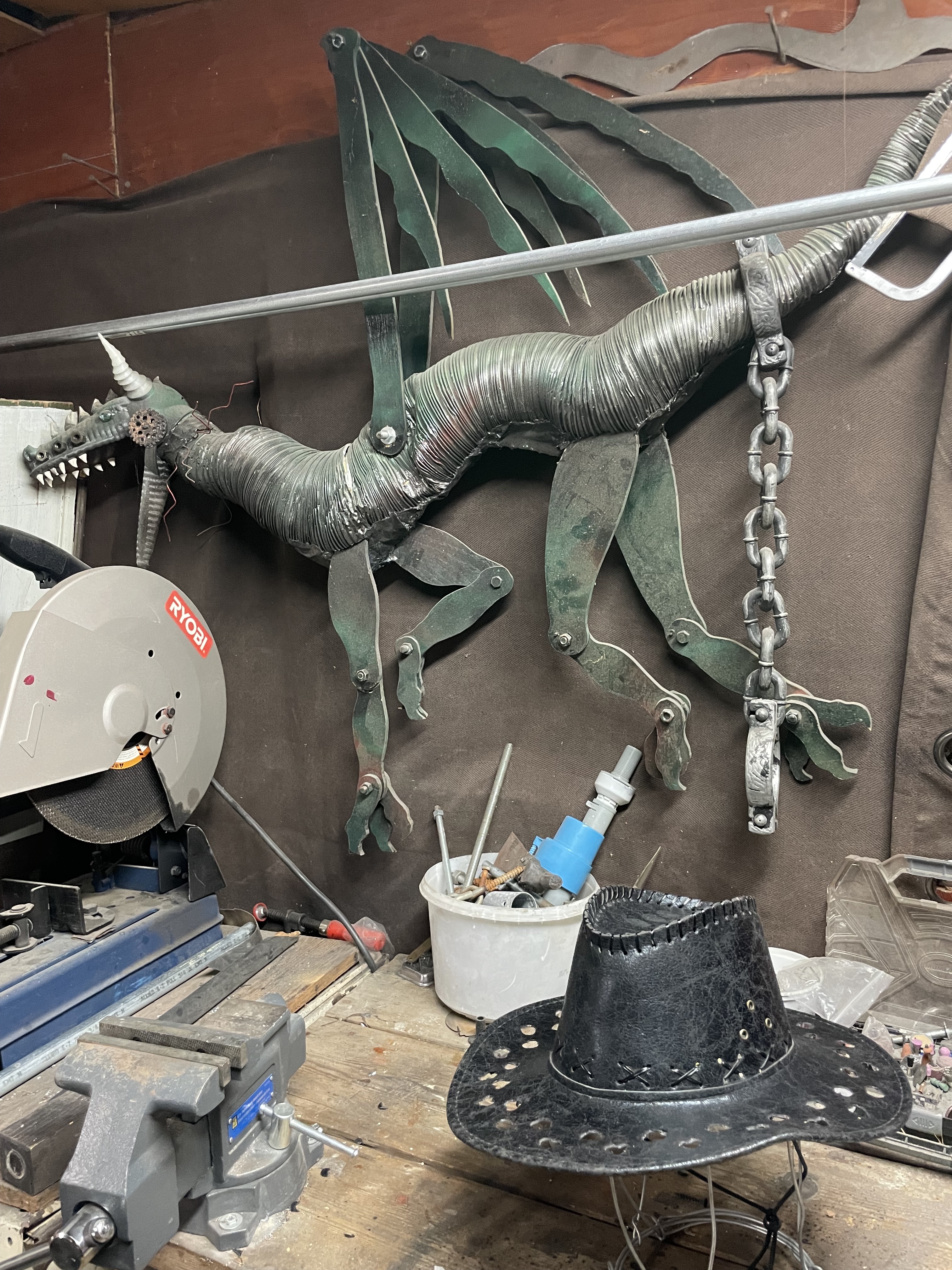 The initial stages of construction the hat, with holes bored out, in the setting of my step-dad's garage. There is a large, metal dragon that occupies the bulk of the space within the backdrop of the photo.